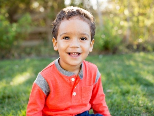 Young boy in red shirt smiling outdoors