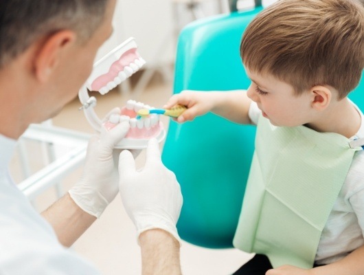 Child brushing teeth in model of smile at dental office