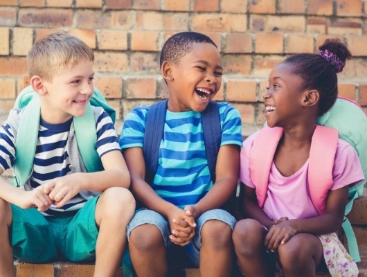 Three laughing kids wearing backpacks