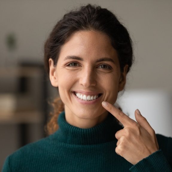 Woman pointing to her smile after cosmetic dentistry in Denton