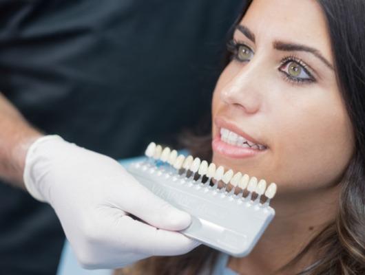 Cosmetic dentist holding row of veneers in front of smile of a patient