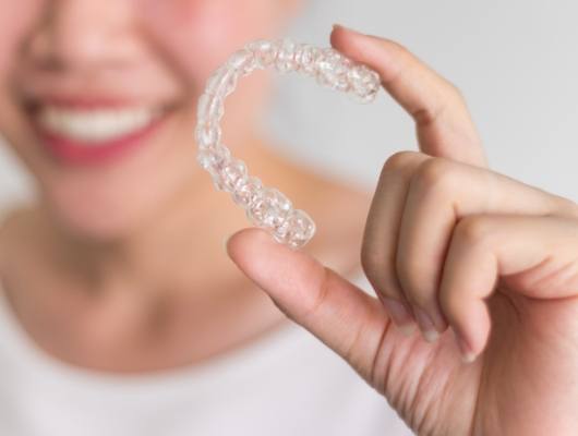 Smiling person holding an Invisalign clear aligner
