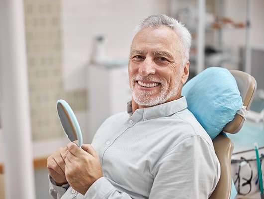 Senior man smiling while holding handheld mirror