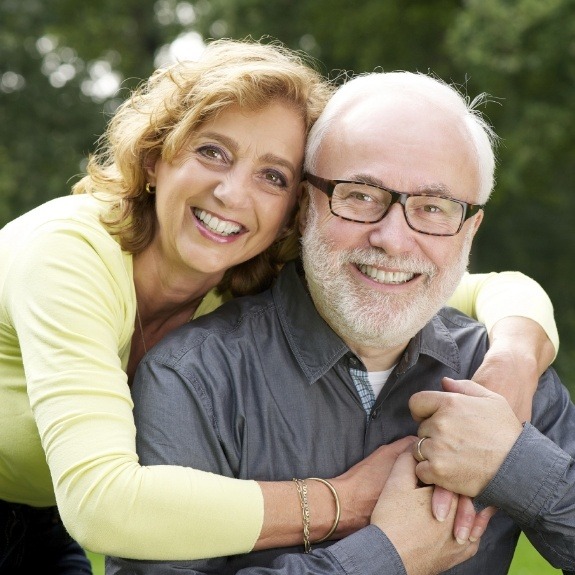 Older man and woman holding each other and smiling with dental bridges in Denton