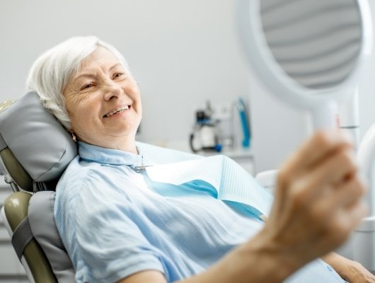 Senior woman in dental chair admiring her smile in mirror