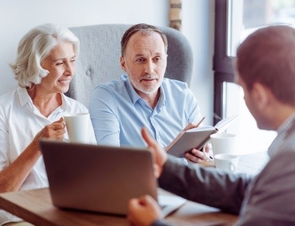 Older man and woman talking to man with laptop at desk