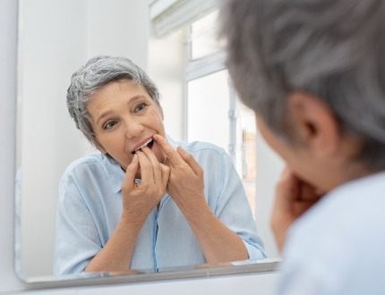 Senior woman flossing her teeth in front of mirror