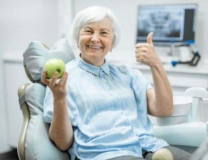 Senior dental patient giving thumbs up and holding green apple
