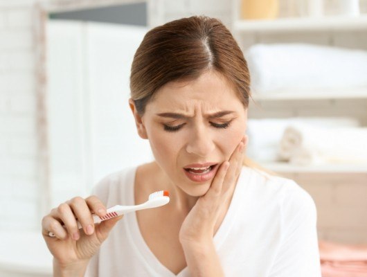 Woman holding her cheek in pain while brushing her teeth