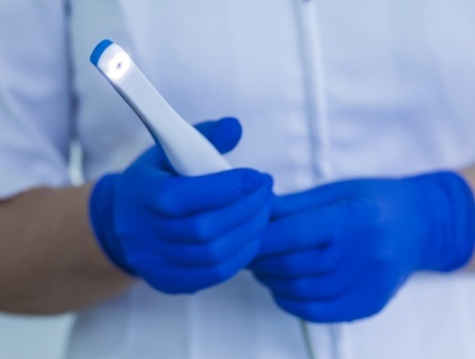 Two gloved hands holding a thin white intraoral camera