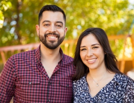 Man and woman smiling with trees in background