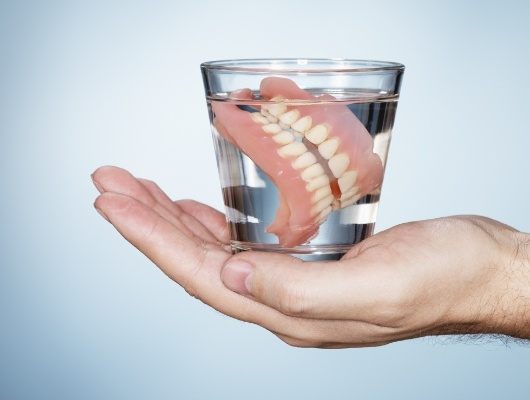 Person holding a glass of water soaking dentures