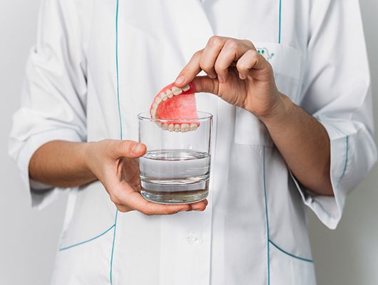 A dentist inserting dentures in Denton into a glass