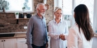 Woman shaking hands with senior woman next to senior man