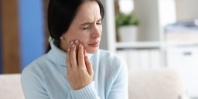 Woman in light blue blouse holding her cheek in pain