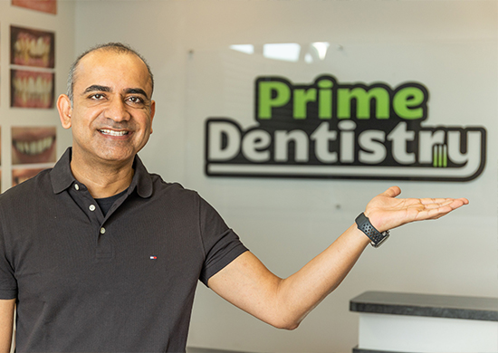 Doctor Ahir gesturing to Prime Dentistry sign on wall