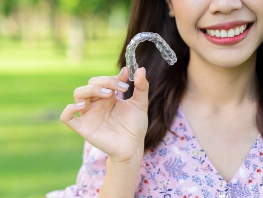 Smiling woman holding Invisalign clear aligner outdoors