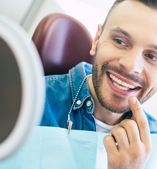 A man using a hand mirror to admire his treated smile