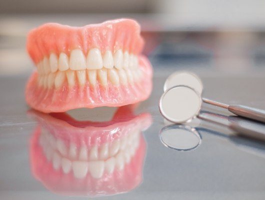Set of full dentures on table next to dental mirror