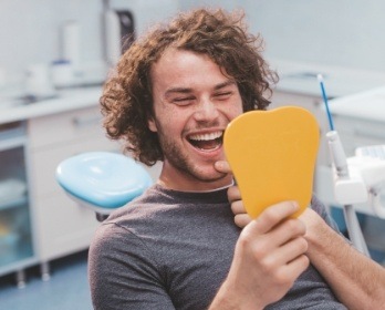 Young man in dental chair looking at his smile in yellow mirror