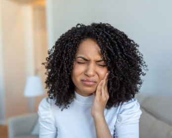 Woman in light blue blouse holding her cheek in pain