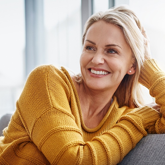 Woman in yellow shirt sitting on couch and smiling after full mouth reconstruction in Denton, TX