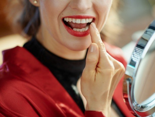 Woman with red lipstick admiring her smile in mirror