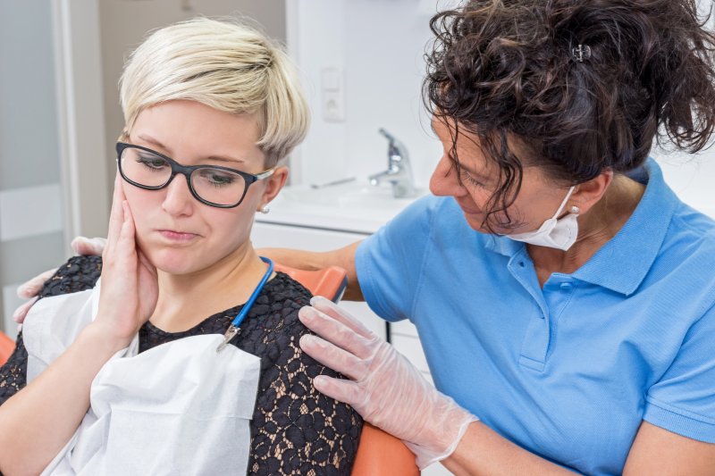 a woman holding her cheek in pain while seeing her emergency dentist