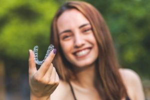 woman smiling and holding a clear aligner in hand